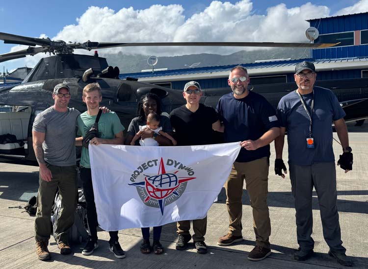 Project DYNAMO team and a family holding the DYNAMO flag beside a helicopter